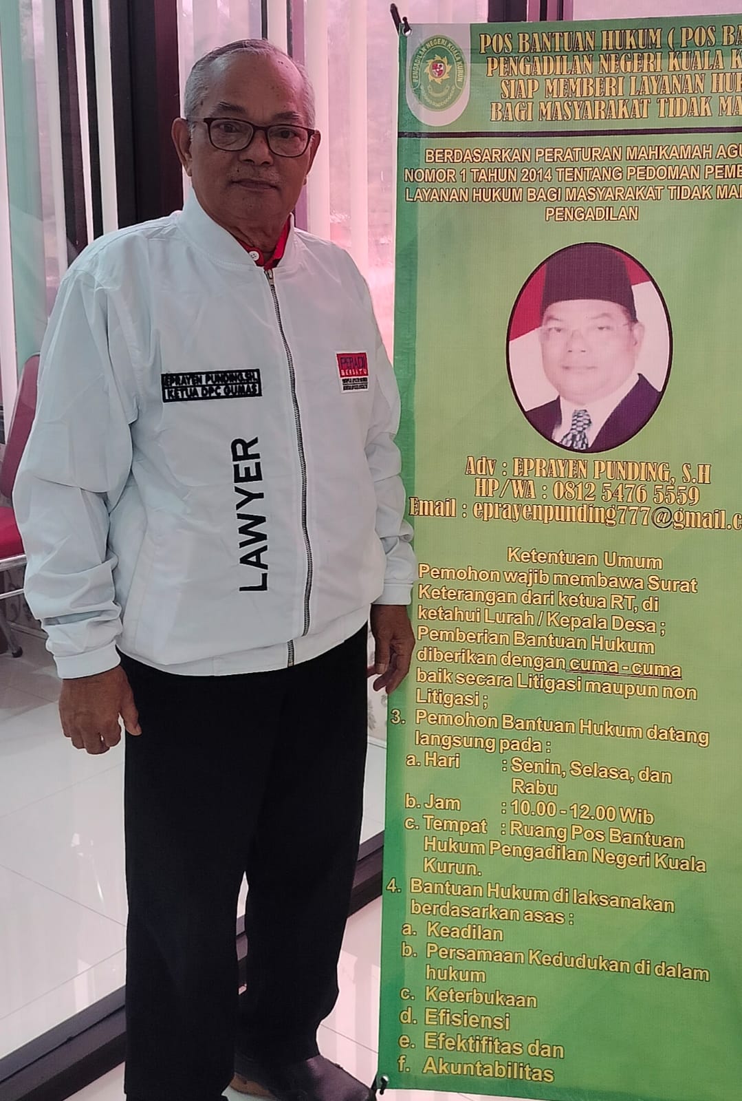 Eprayen Punding, S.H. Berdiri di Samping Banner Program Pos Bantuan Hukum